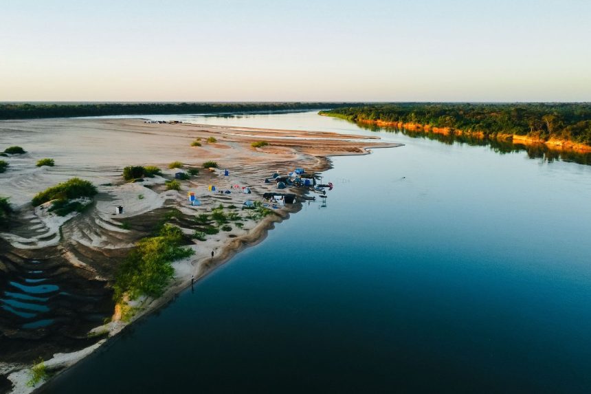 Vista aérea do rio Araguaia, com um acampamento às margens e vegetação ao redor.