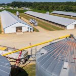 Vista aérea de uma grande instalação agrícola com silos, armazéns e caminhões.